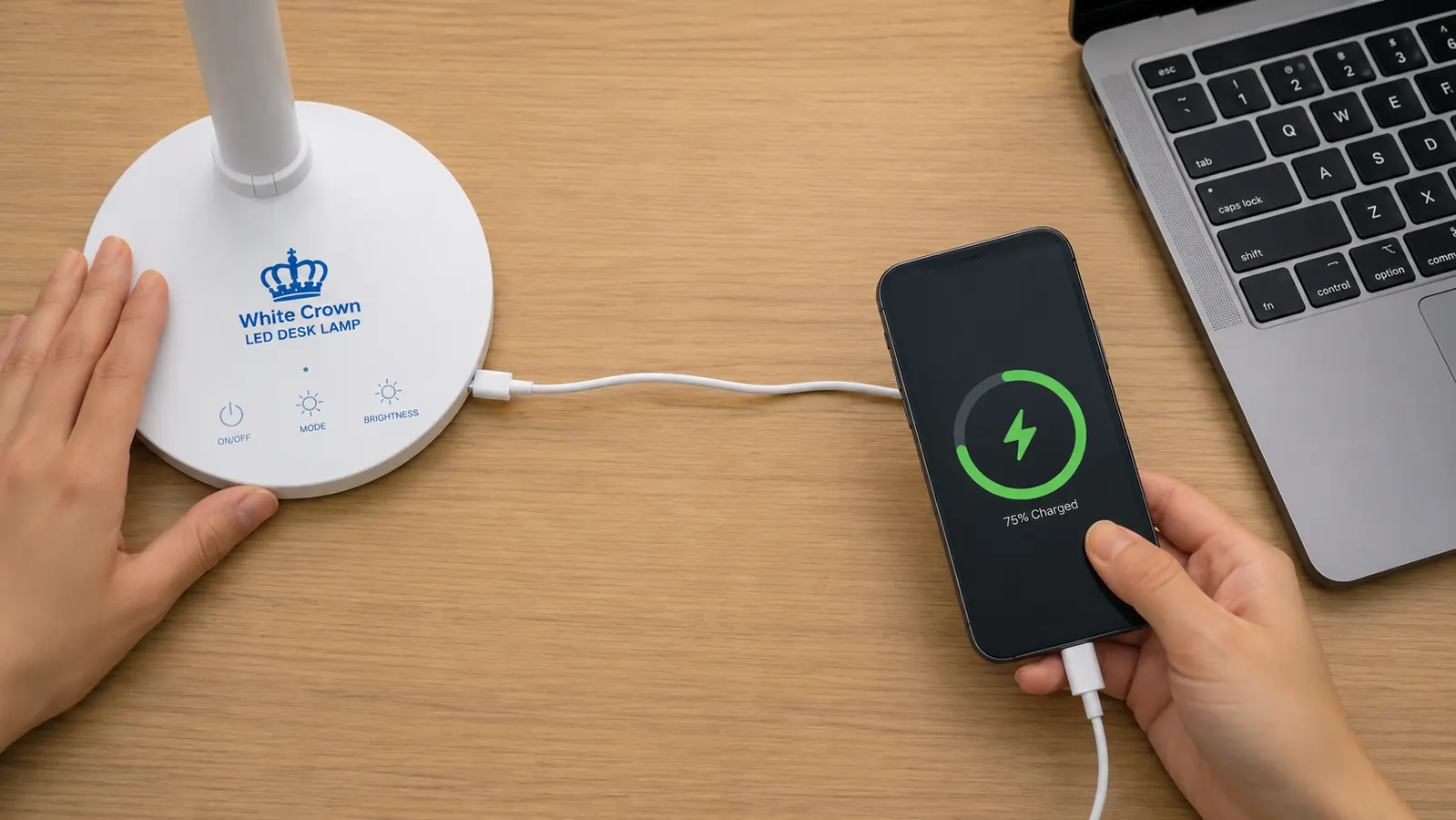 White Crown LED desk lamp base sitting on a cluttered desk next to a laptop trackpad and a charging cable running sideways to the USB port